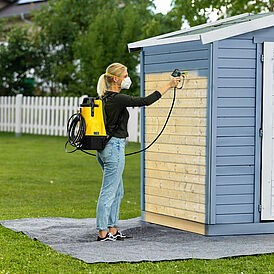 Blonde Frau sprüht Gartenhaus blau mit Farbsprühgerät Control Pro 300 Move 18 V